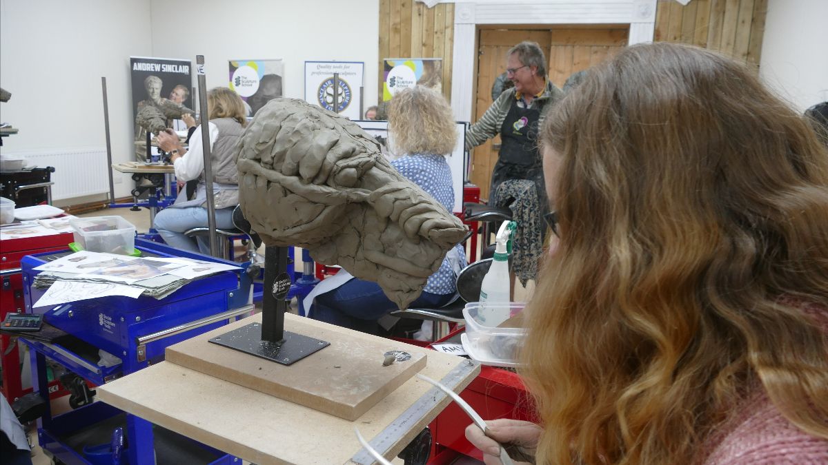 woman sitting in a classroom with a clay model of an animal's head in progress