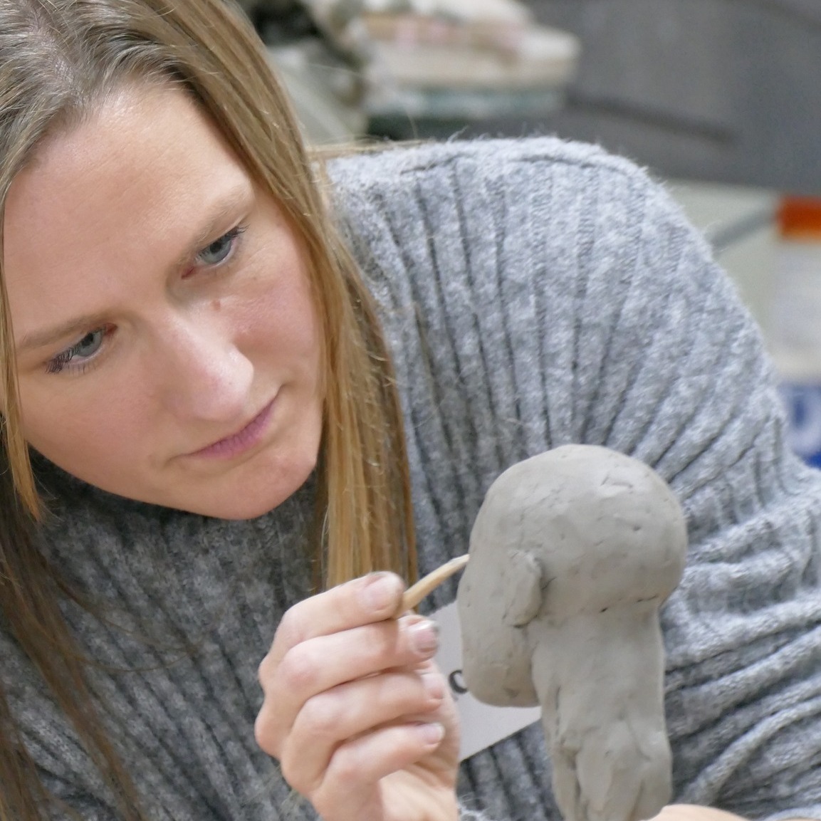 woman concentrating on small clay sculpture of a human head